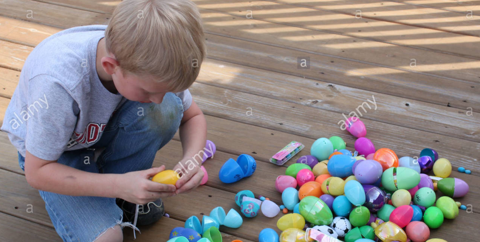 A child opens a plastic easter egg, with numerous plastic eggs strewn around beside him.