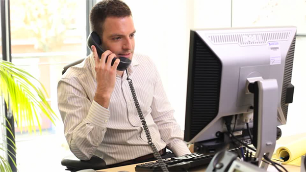 A man at his computer desk speaking on the phone, presumably to the post office